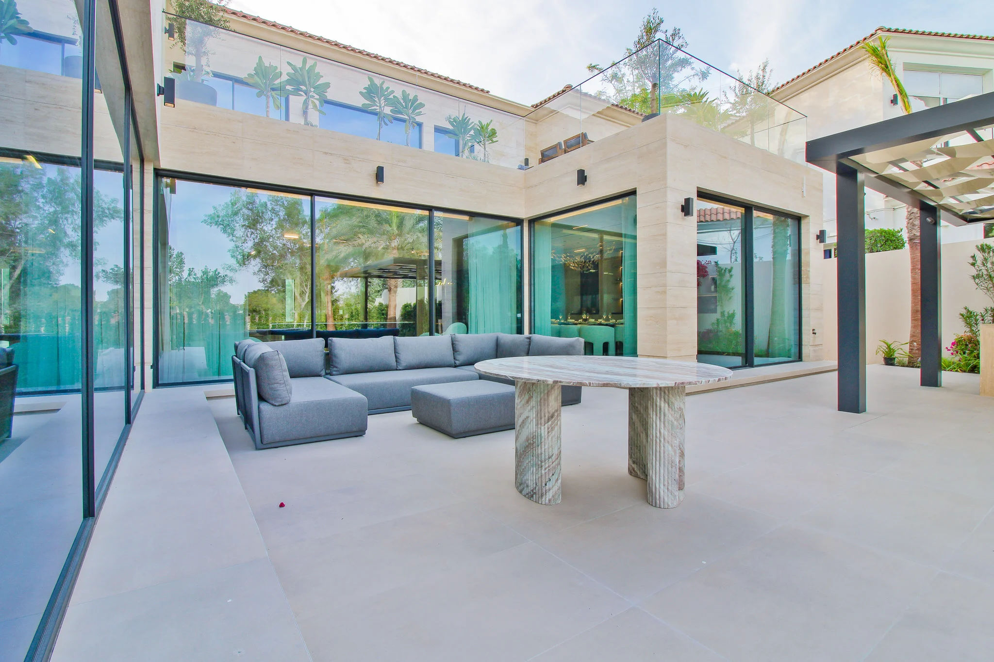 Travertine courtyard terrace with a marble table and grey seating, framed by full-height glass