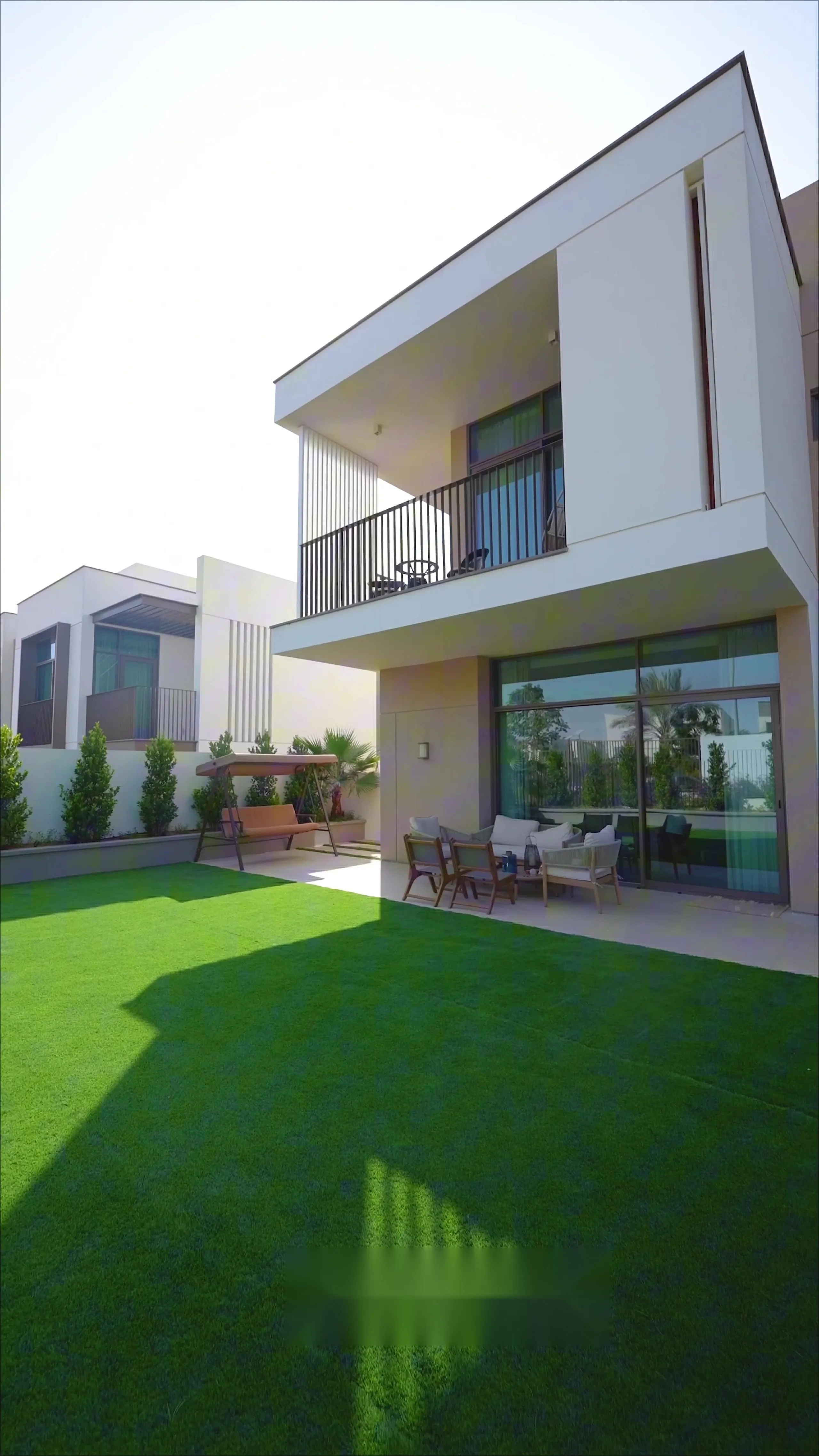 Finished villa rear elevation with a first-floor balcony, covered terrace seating and a manicured lawn