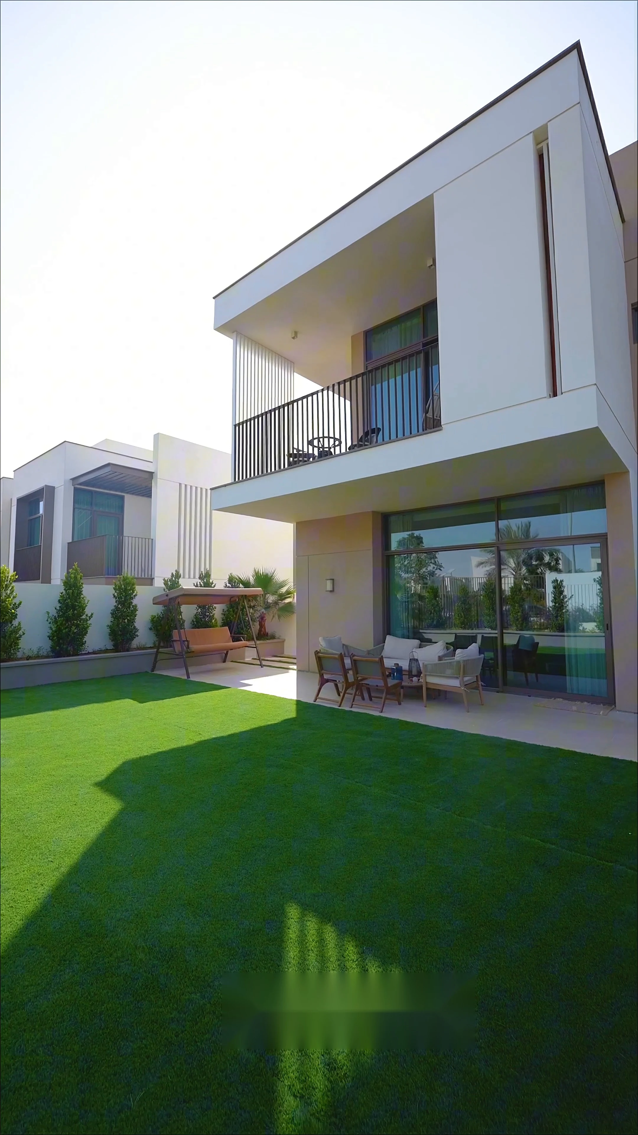 The finished villa — a two-storey contemporary elevation with a first-floor balcony, covered terrace and a manicured lawn
