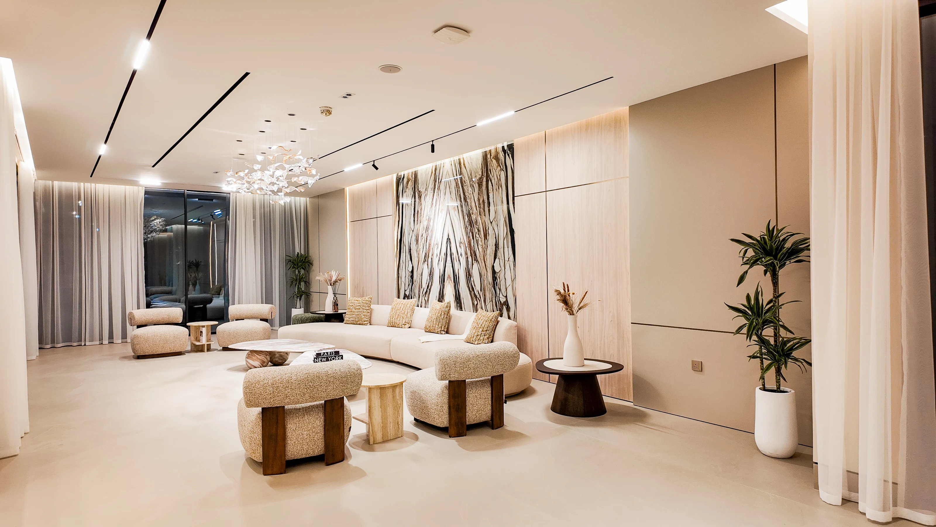Formal lounge with a book-matched marble panel, curved seating and a sculpted glass chandelier, lit for the evening