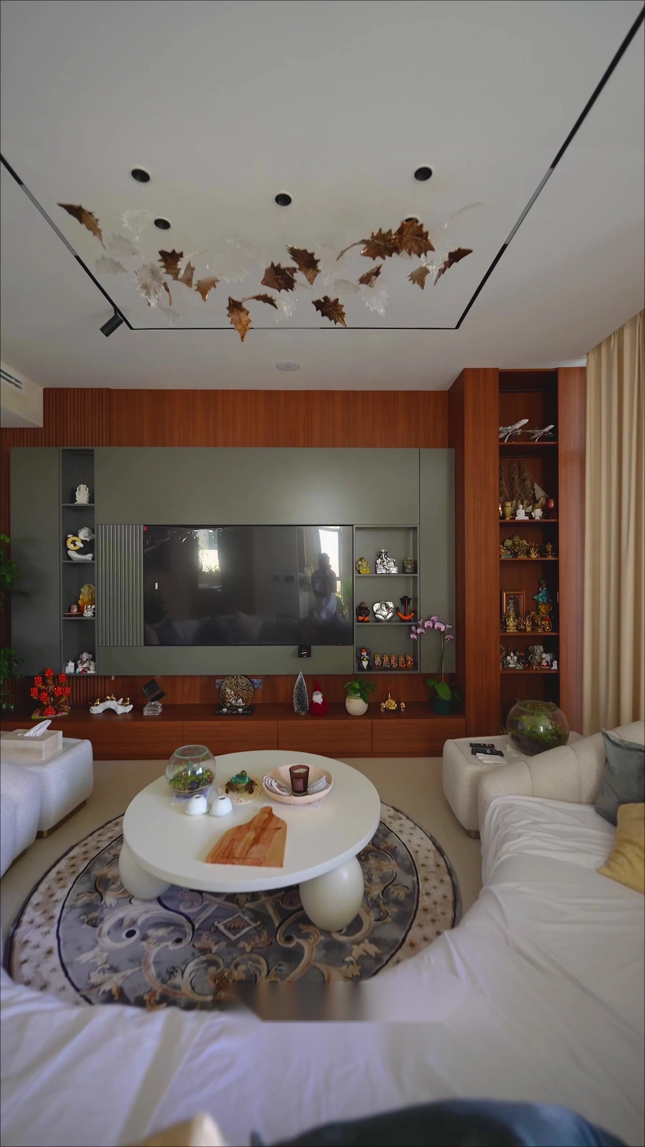 Finished living room with a curved boucle sofa, walnut media wall and a sculptural gilt-leaf ceiling installation