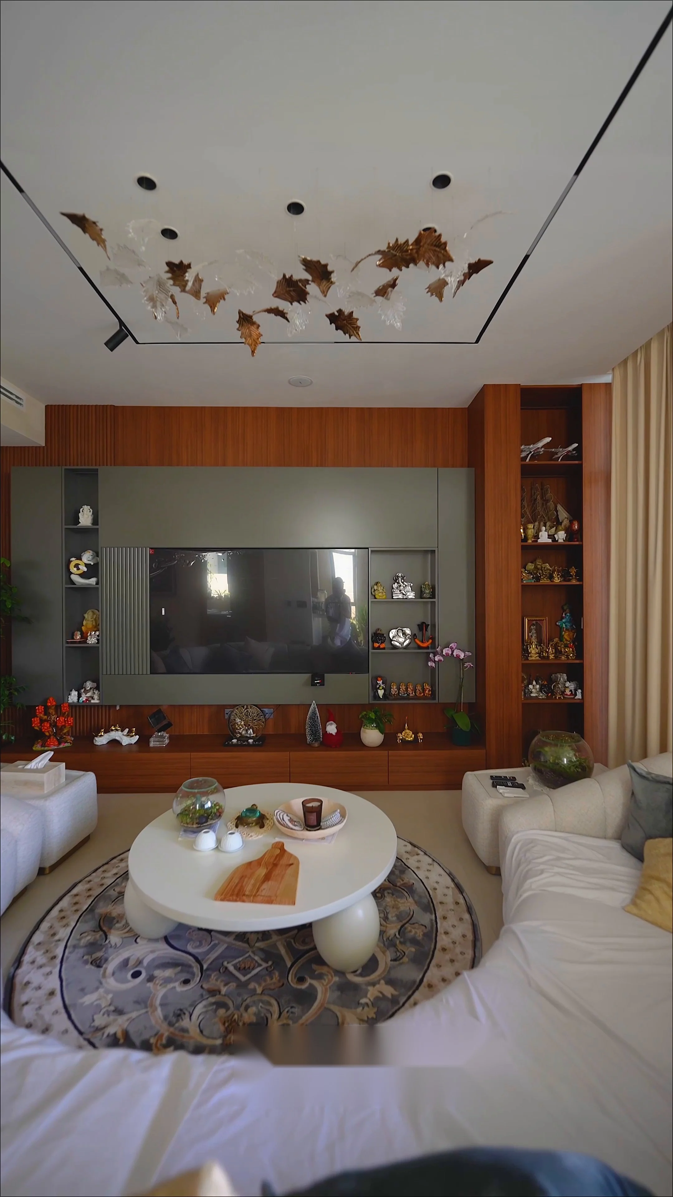 Finished living room with a curved boucle sofa, walnut media wall and a sculptural gilt-leaf ceiling installation