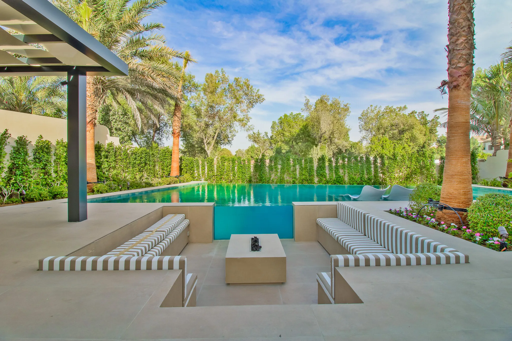 Infinity pool with sunken striped seating around a fire table, framed by palms