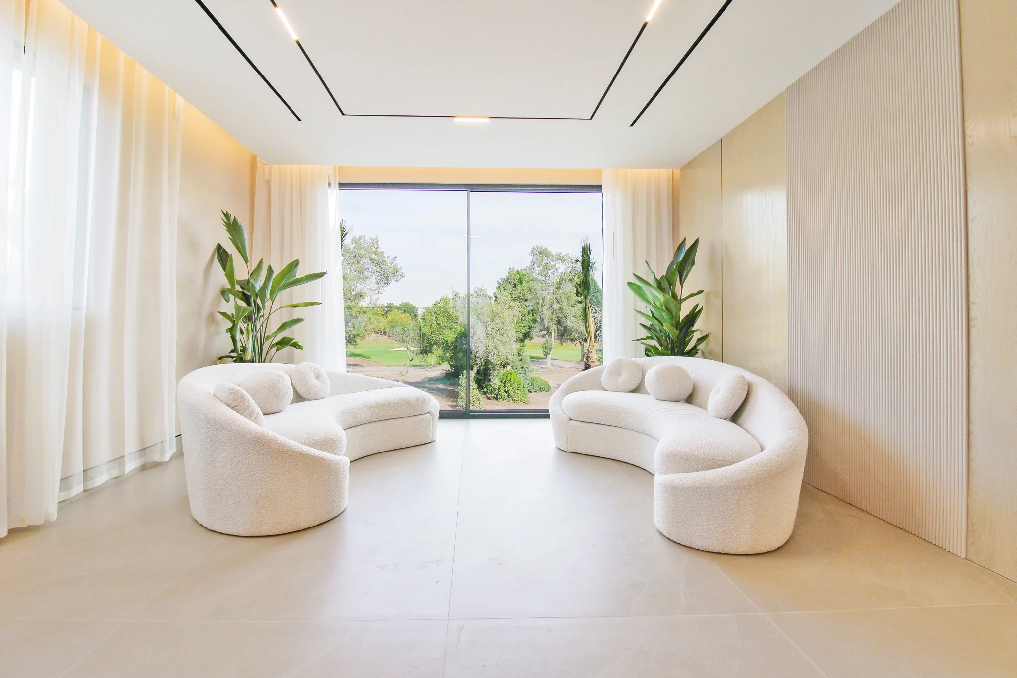 Sitting room with curved boucle sofas facing a full-height window onto the golf course