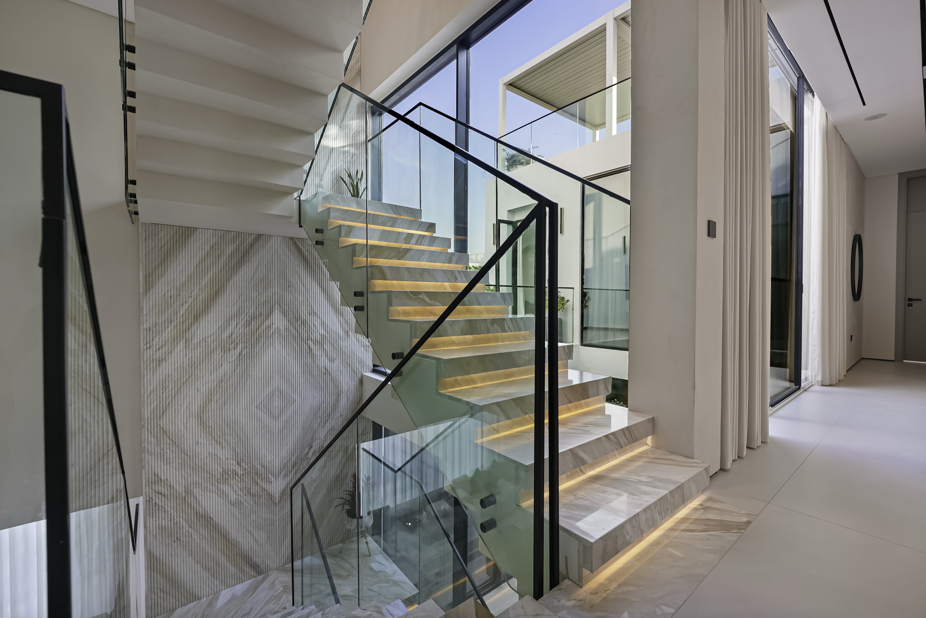 Book-matched marble staircase with under-lit treads and glass balustrades, Al Barari villa