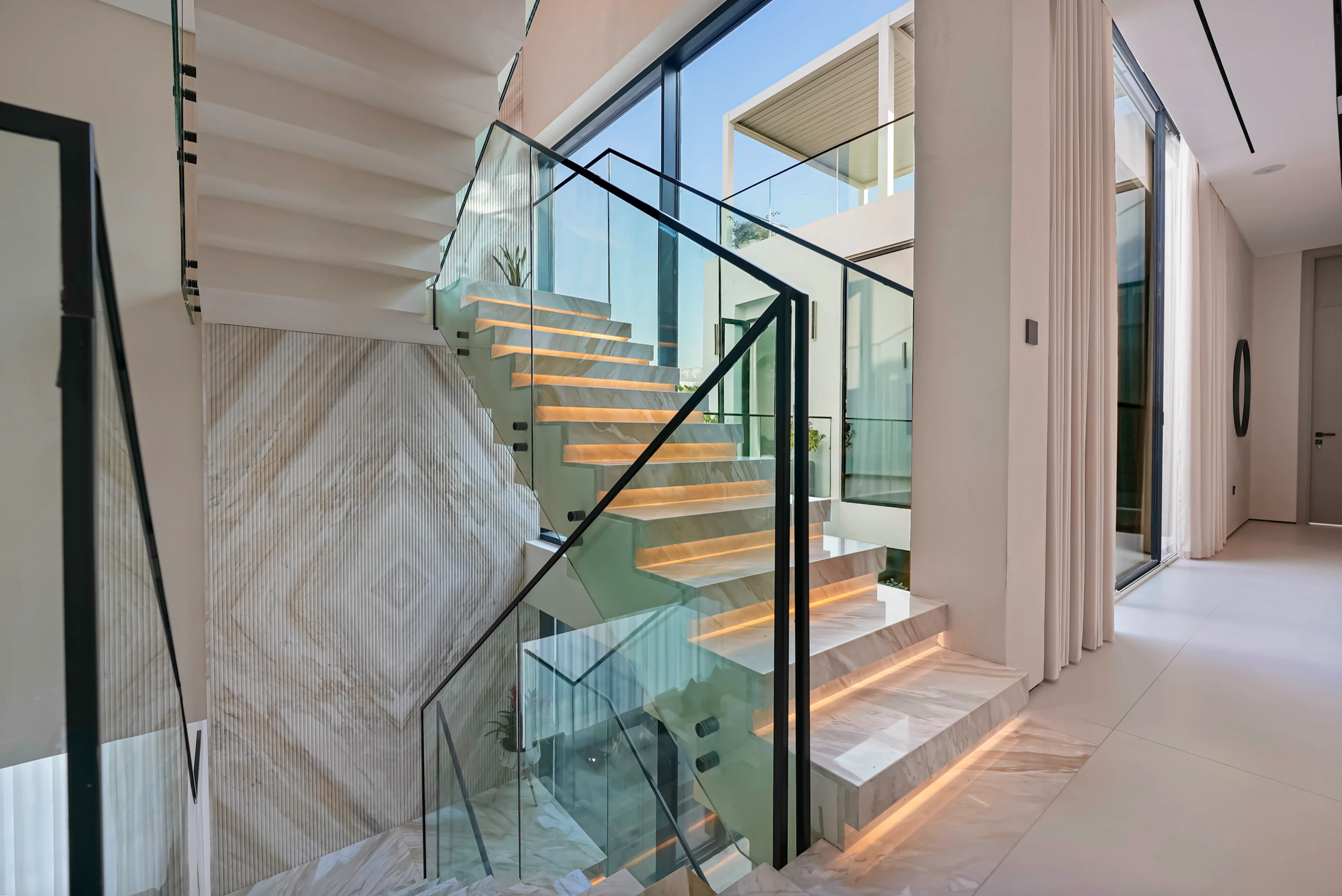 Floating marble staircase with under-lit treads and glass balustrades, rising past a fluted stone wall